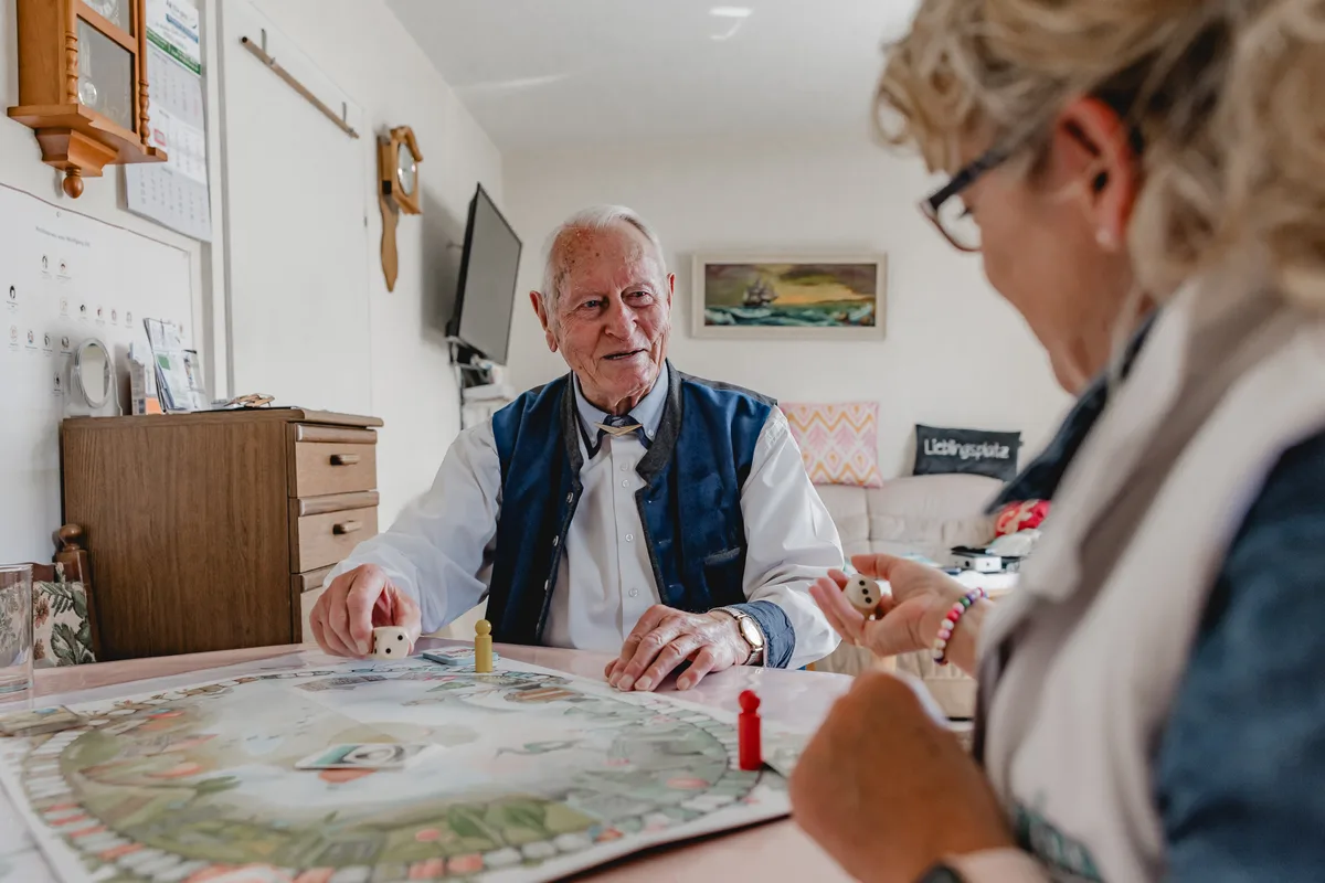 REKA Pflegekraft spielt ein Brettspiel mit einem Senior zu Hause